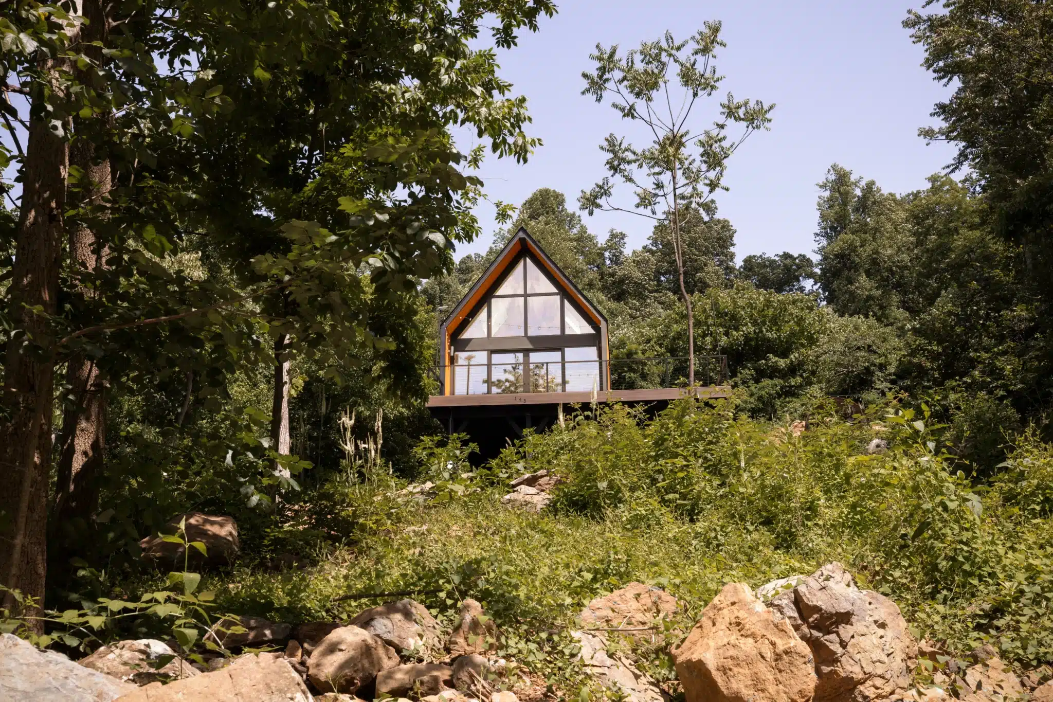 Modern secluded cabin exterior with floor-to-ceiling windows and elevated deck surrounded by Virginia forest