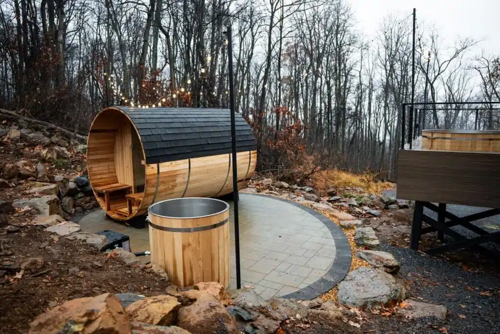 Barrel sauna and soaking tub contrast therapy setup on stone patio in Virginia forest retreat
